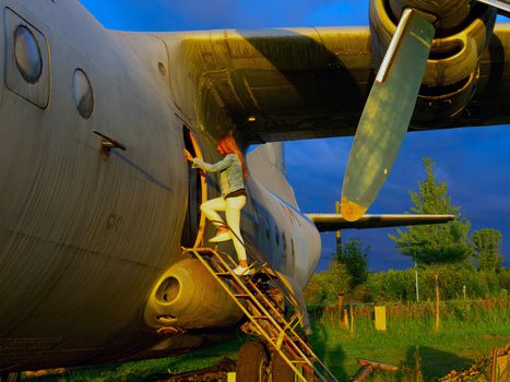 Yo ungwoman standing at plane ladder going to board, outdoors, airport. Old Soviet military airplane, sunset time. Close up of a Abandoned Historic Aircraft. Close up of propeller engine.