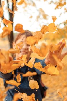happy child playing with leaves in autumn in the forest. Girl Throwing Dry Leaves into Camera.Seasonal Outdoor Activities with Children. Capture lifestyle on a walk.