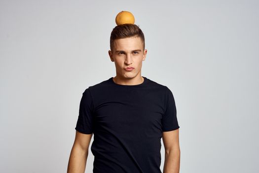 A guy with an orange in his hand and in a black T-shirt on a light background cropped view. High quality photo