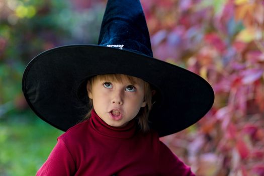Little girl in witch costume making different faces on halloween party in the garden