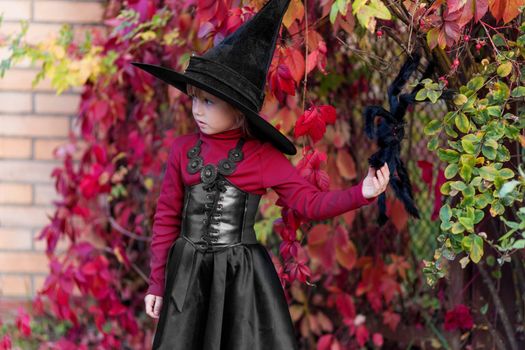 Little girl in witch costume posing on halloween party in the garden.