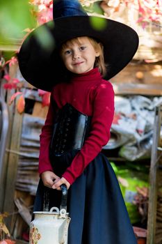 Little girl dressed as a witch holding a kettle on halloween party in the garden