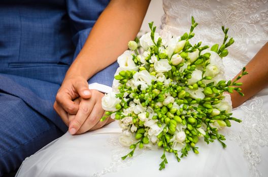 Bride and groom, hand in hand at the wedding ceremony with the flower bouquet in the foreground