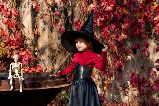 Little girl in a witch costume interferes with a potion on a halloween party in the garden