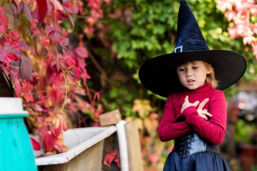 Little girl in witch costume posing on halloween party in the garden.