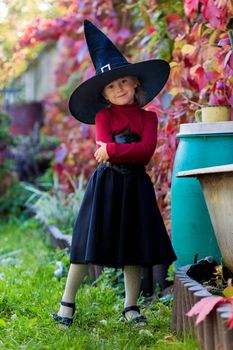 Little girl in witch costume posing on halloween party in the garden.