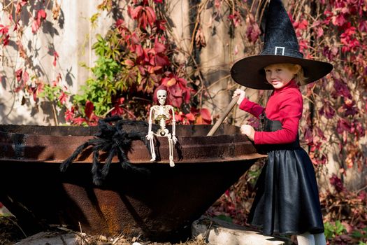 Little girl in a witch costume interferes with a potion on a halloween party in the garden