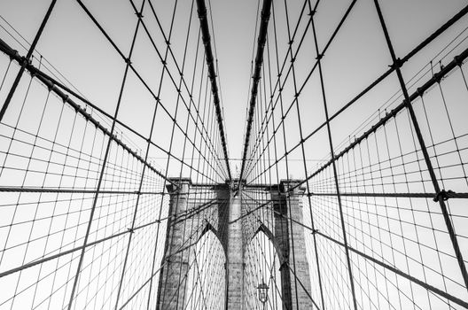 Black and white low angle view of the web of cables of Brooklyn bridge in a sunny afternoon on a blue sky as background