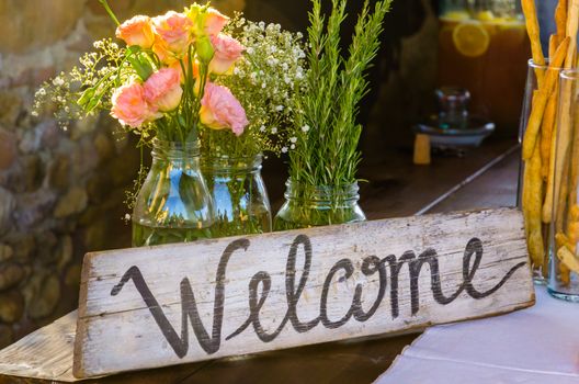 Welcome sign painted on wood next to a bunch of pink flowers