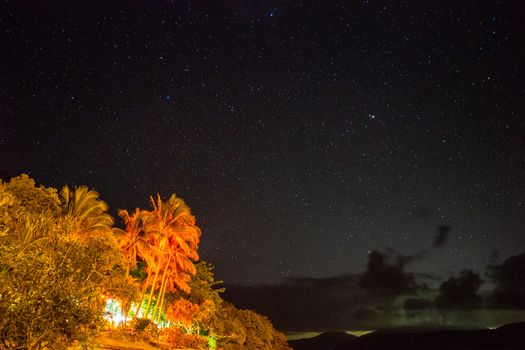 Starry night sky from Fitzroy Island beach illuminated by the resort colourful lights. Queensland, Australia. 