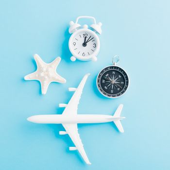 World Tourism Day, Top view flat lay of minimal toy model plane, airplane, starfish, alarm clock and compass, studio shot isolated on a blue background, accessory flight holiday concept