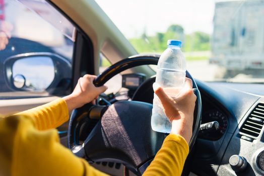 Asian woman holding a water bottle for drink while driving the car in the morning during going to work on highway road, Transportation and vehicle concept