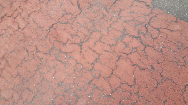 Red colored damaged road or paved pathway with crackes of different shpaes. Cracked texture with copy space for text and messages