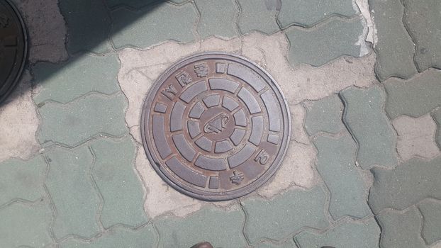 Chuncheon, South Korea- May-2, 2019: Top view of a manhole cover on drainage or sewerage under paved road.