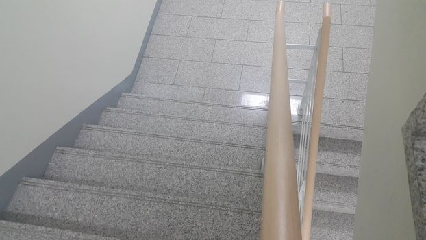 Closeup view of wooden handrail of grey concrete stairs in a modern building. Handrails help people avoiding accidents while moving on stairs.