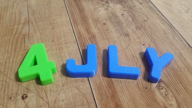 Plastic colored alphabets making words 4 july are placed on a wooden floor. These plastic letters can be used for teaching kids.