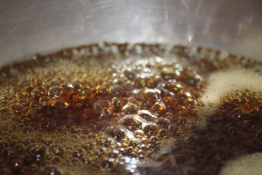 Closeup macro photograph with selective focus of boiling brown water in a metal pan for brewing tea