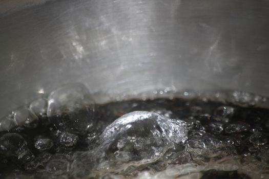 Closeup macro photograph with selective focus of boiling water in a metal pan