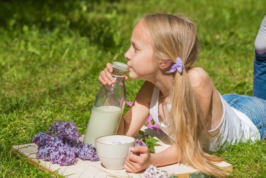 Little blonde girl with cup of milk on nature. Products for human health. Healthy food. World milk day.