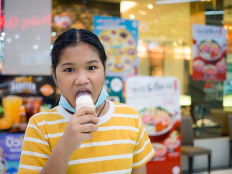 Little girl eating ice cream inside the mall with blurred background.