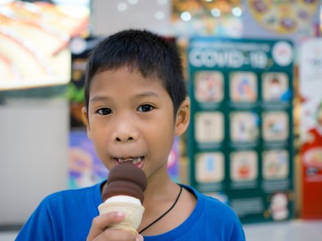 A boy eating ice cream inside a mall with a blurred background.