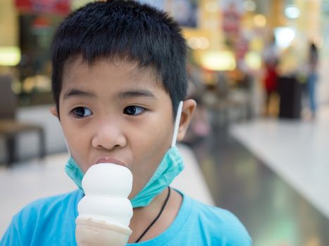 A boy eating ice cream inside a mall with a blurred background.