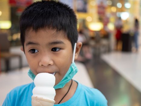 A boy eating ice cream inside a mall with a blurred background.