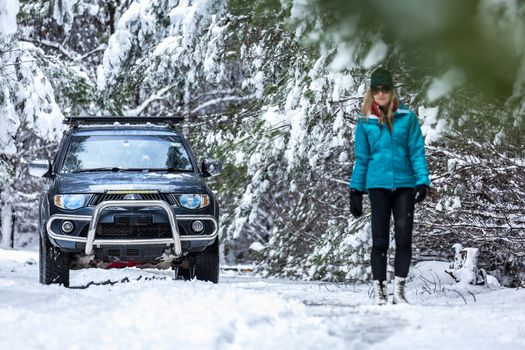 A woman outside  in snow covered pine forest with 4wd ute