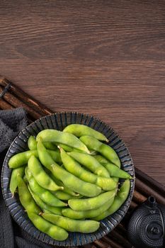 Top view of fresh cooked boiled edamame in a plate on wooden tray and table background with copy space, healthy protein food concept.