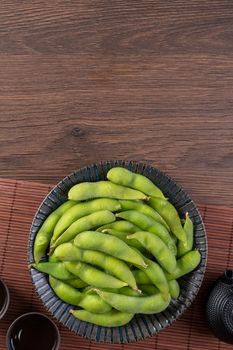 Top view of fresh cooked boiled edamame in a plate on wooden tray and table background with copy space, healthy protein food concept.