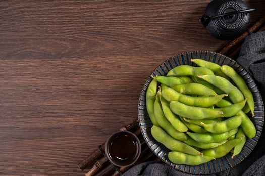 Top view of fresh cooked boiled edamame in a plate on wooden tray and table background with copy space, healthy protein food concept.