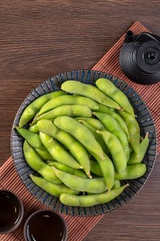 Top view of fresh cooked boiled edamame in a plate on wooden tray and table background with copy space, healthy protein food concept.