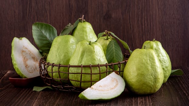 Close up of delicious beautiful guava set with fresh green leaves isolated on dark wooden table background.