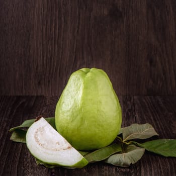 Close up of delicious beautiful guava set with fresh green leaves isolated on dark wooden table background.