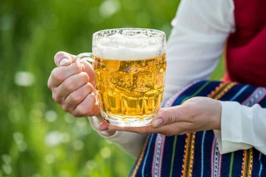 Glass of light beer in the hands of a Latvian woman traditional clothing. Preparing Ligo festival. Riga. Latvia