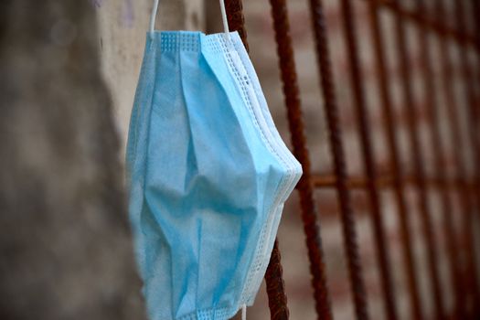 Blue surgical mask used for Covid-19 and discarded in a park lying on a rusty grate
