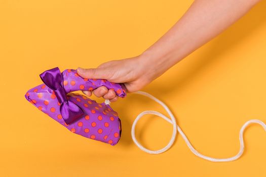 Female hand holding an iron wrapped in purple gift paper on a orange background