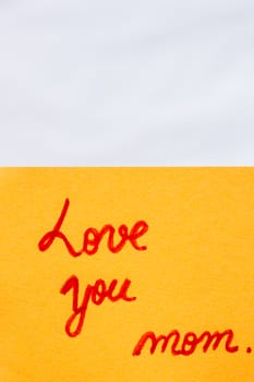 Love you mom handwriting text close up isolated on orange paper with copy space. Writing text on memo post reminder.