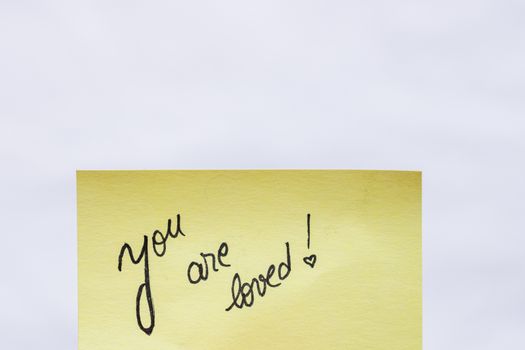 You are loved handwriting text close up isolated on yellow paper with copy space.