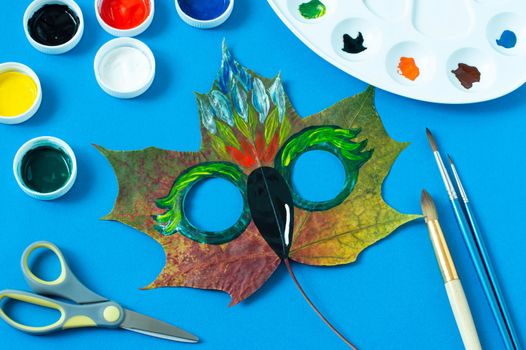 Mask painted on maple leaf. Drawing on autumn leaves. Parrot mask for autumn carnival or party. Art project for children. DIY concept