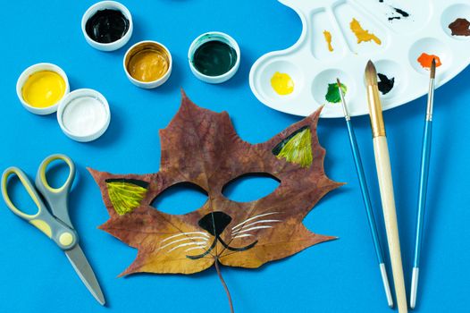 Mask painted on maple leaf. Drawing on autumn leaves. Cat Fox mask for kids autumn carnival or party. Art project for children. DIY concept