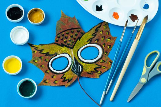 Mask painted on maple leaf. Drawing on autumn leaves. Owl mask for kids autumn carnival or party. Art project for children. DIY concept