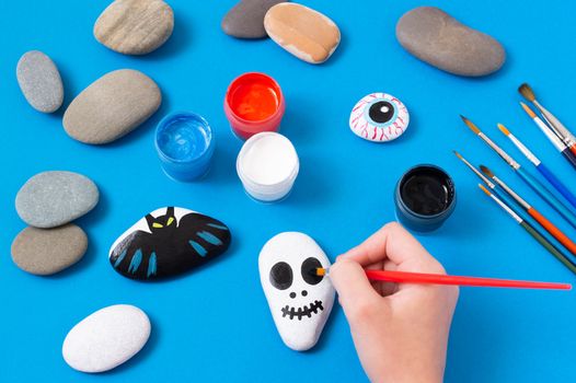 Drawing on stones Halloween characters. Art project for children. DIY concept. Halloween party decor. Skull painted on sea stone