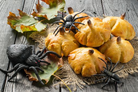 Homemade sweet pumpkin buns. Original baking in form of pumpkin and black toy spiders. Symbols Halloween. Idea of design meal for Halloween party. Scary and funny Halloween food 
