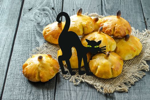 Homemade sweet pumpkin buns. Original baking in form of pumpkin and black cat made of paper. Symbols and characters Halloween. Idea of design meal for Halloween party. Scary and funny Halloween food 