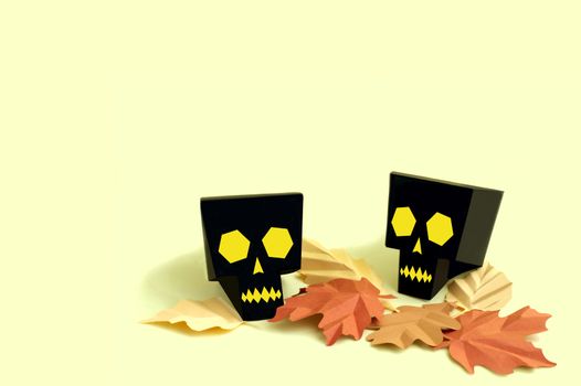 Volumetric paper skulls with autumn leaves on yellow background. Paper art and craft. Festive Halloween concept. Copy space