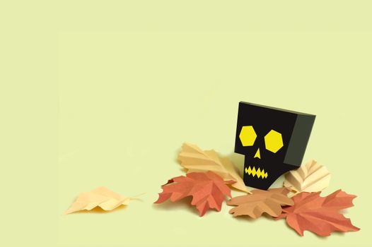 Volumetric paper skull with autumn leaves on yellow background. Paper art and craft. Festive Halloween concept. Copy space