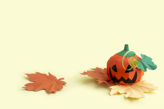 Volumetric paper Jack-o-lantern with autumn leaves on yellow background. Paper art and craft. Festive Halloween concept. Copy space