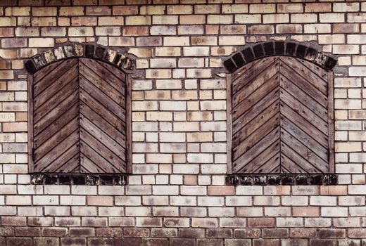 Two windows with closed wooden shutters on a brick wall background