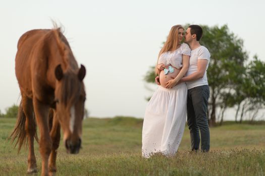 A farmer with his pregnant wife at sunset on his farm. Posing with a horse.